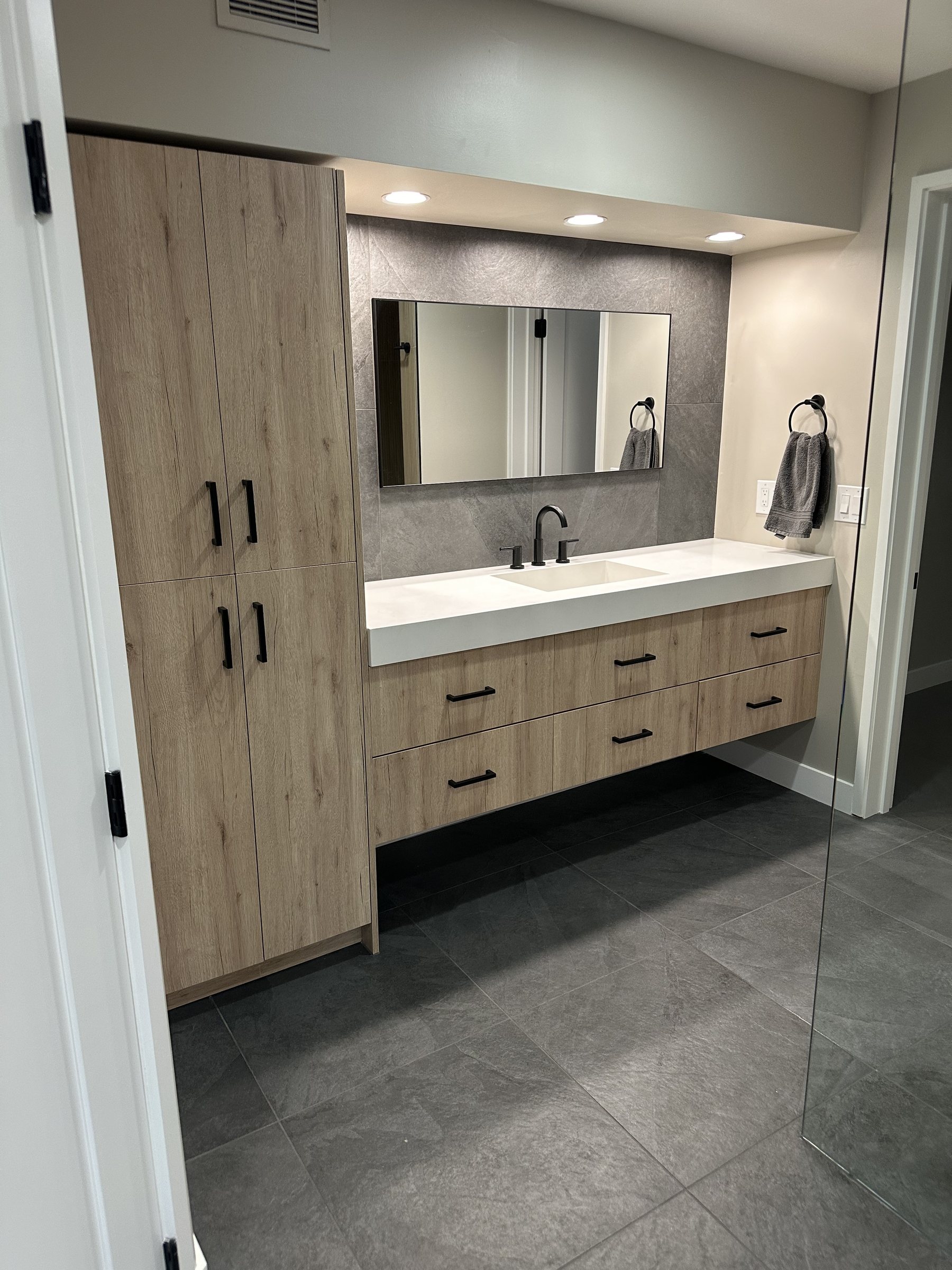 Floating wood vanity with tall linen tower and black hardware in a Phoenix bathroom remodel